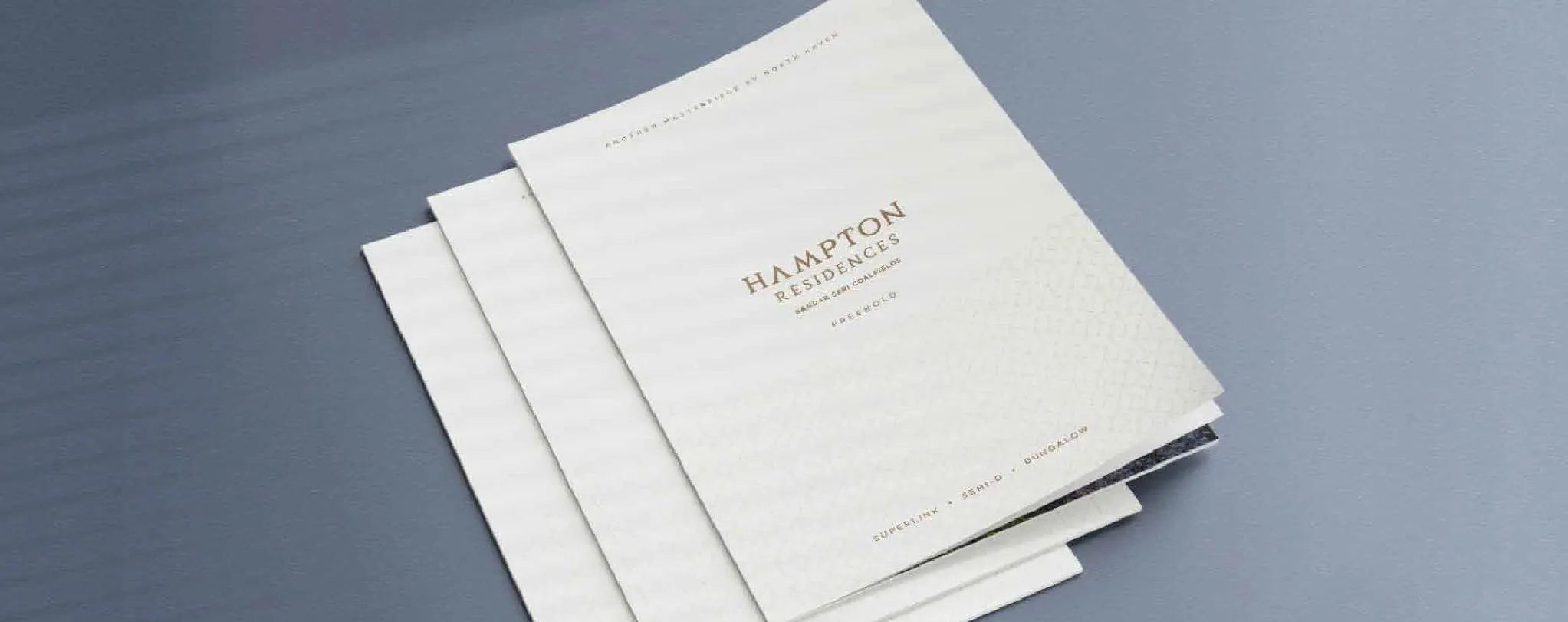Foil-stamped Hampton Residences brochures from our team's portfolio, fanned on a table